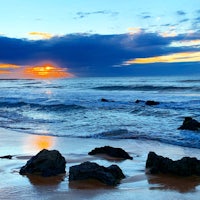 a sunset on a beach with rocks and water